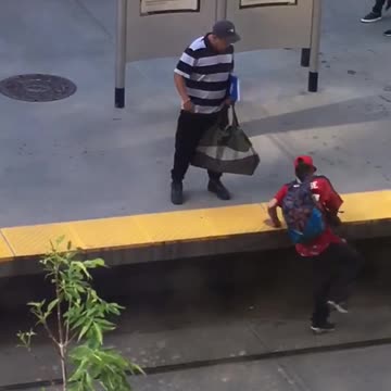Guy in red falls asleep while standing at train station and falls onto tracks striped shirt guy tries to help him