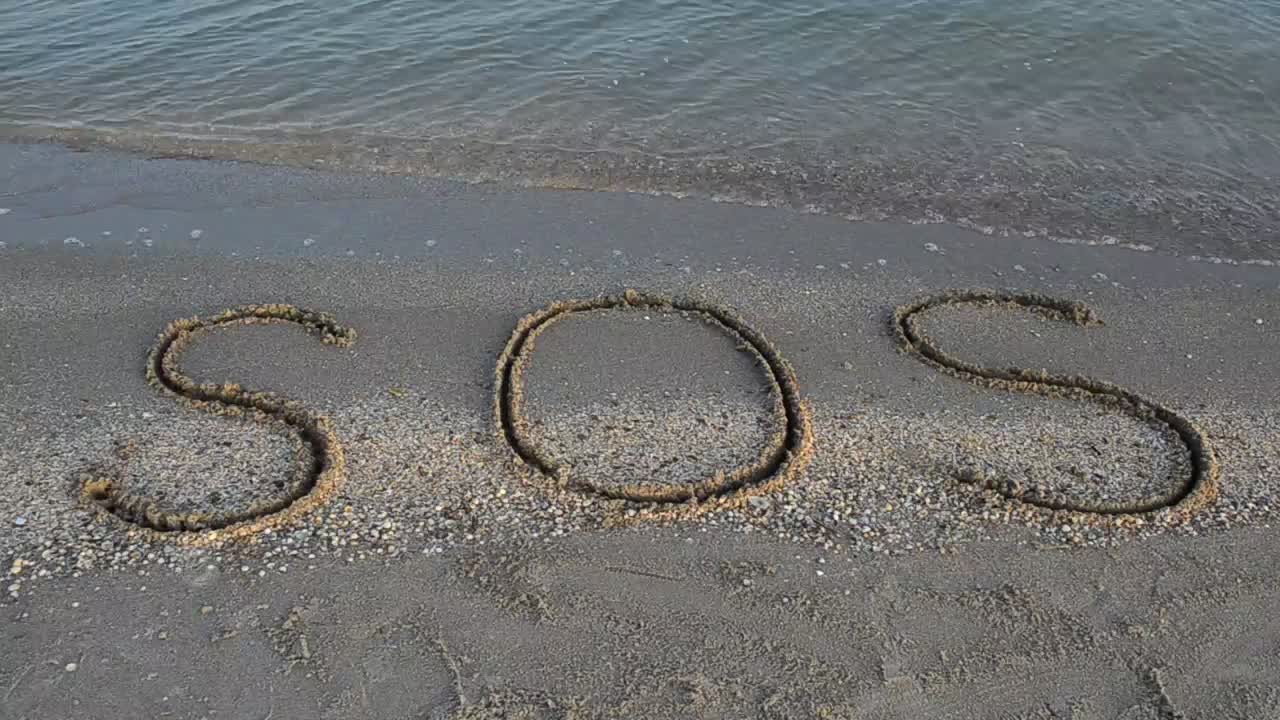 "SOS" written in the sand on the shore of a beach
