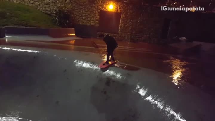 Wetsuit guy rides red boogie board down empty pool hits back head at night