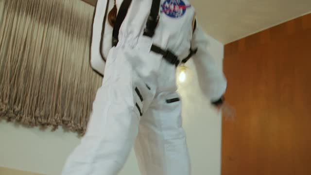 Little girl dressed as an astronaut jumping on the bed