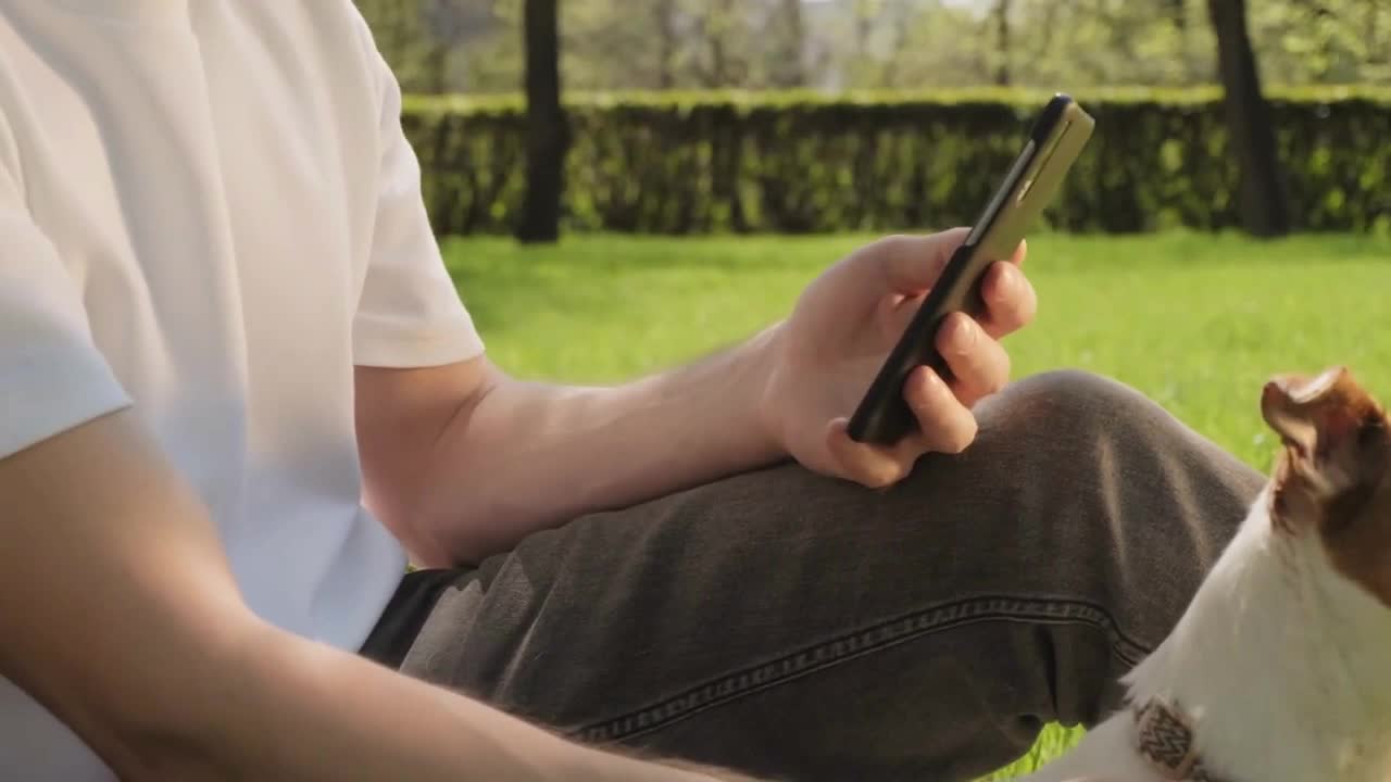 Handheld slowmo tilt up of young man in face mask sitting on green grass in park