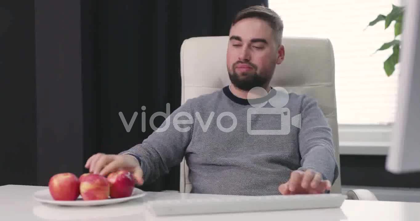 Hungry Man Sitting At Desk Typing On The Keyboard And Eating Apples