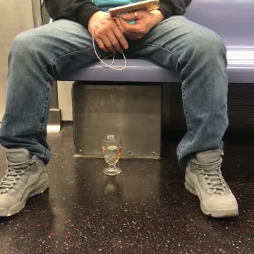 Man has goldfish in class cup on floor of train