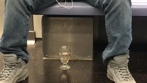 Man has goldfish in class cup on floor of train