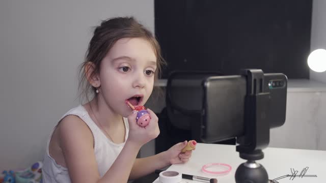 While applying lipstick, a young girl consults her smartphone.
