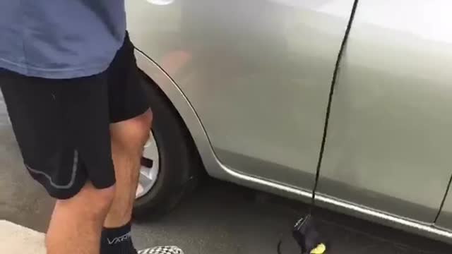 Man in blue stuffs surf board in silver car