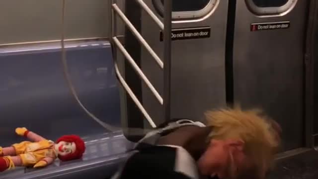 Person wearing donald trump mask screams on the floor on subway train, guy nearby casually on his phone