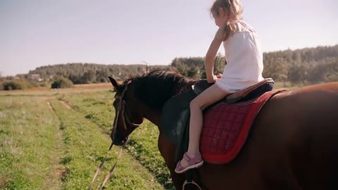 A happy little girl riding a horse in the nature on a sunny day