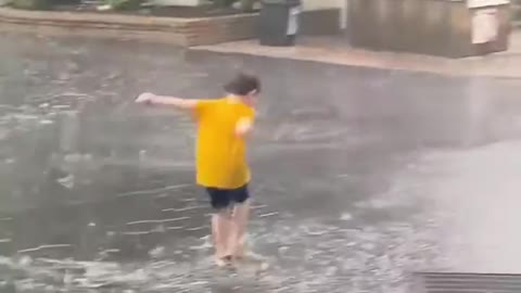 Little Boy Plays In a Water Puddle While It Rains Heavily At Amusement Park