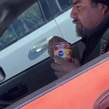 Man is driving car eating a can of dog food