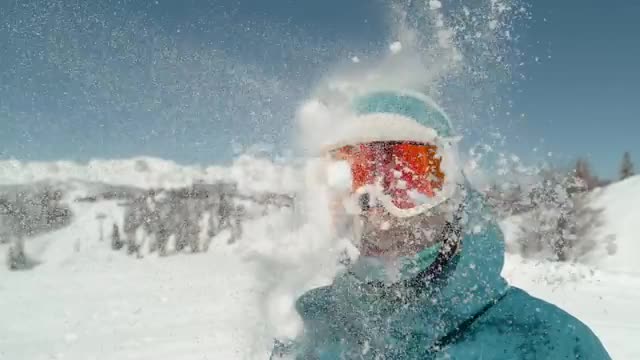 Excited girl wearing ski goggles gets hit in the head by snowbal