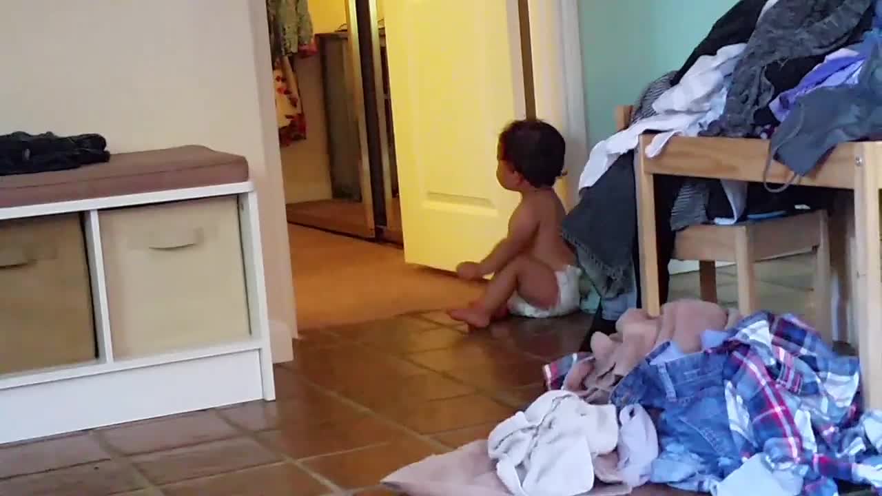 Persistent baby repeatedly puts pants on his head