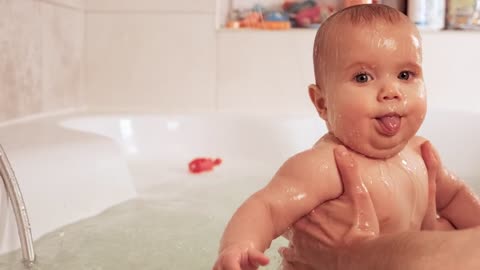 Person holding baby in bathtub with both hands