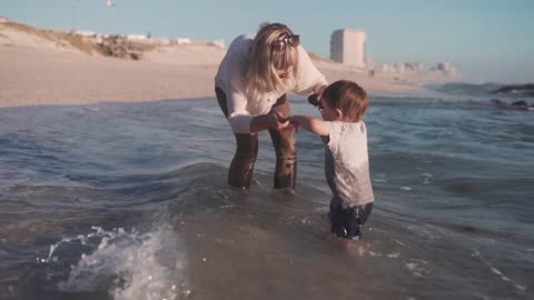 A Mother And Child Standing In The Beach Water Throwing Rocks