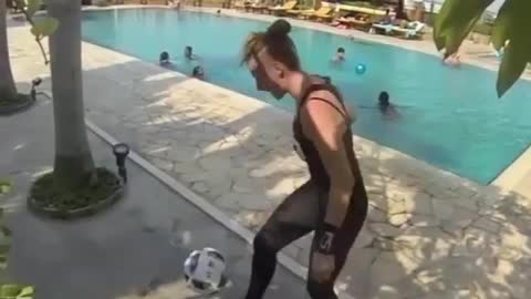 A girl was playing football by herself by the pool