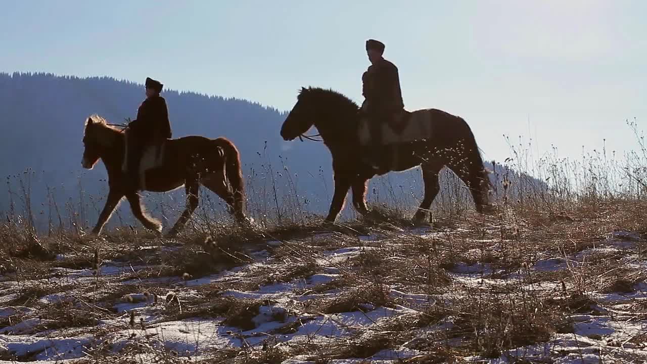 Two horsemen riding on horses through mountainous terrain