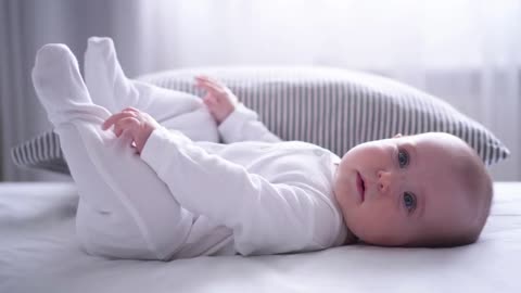 Funny chubby baby playing with feet on bed