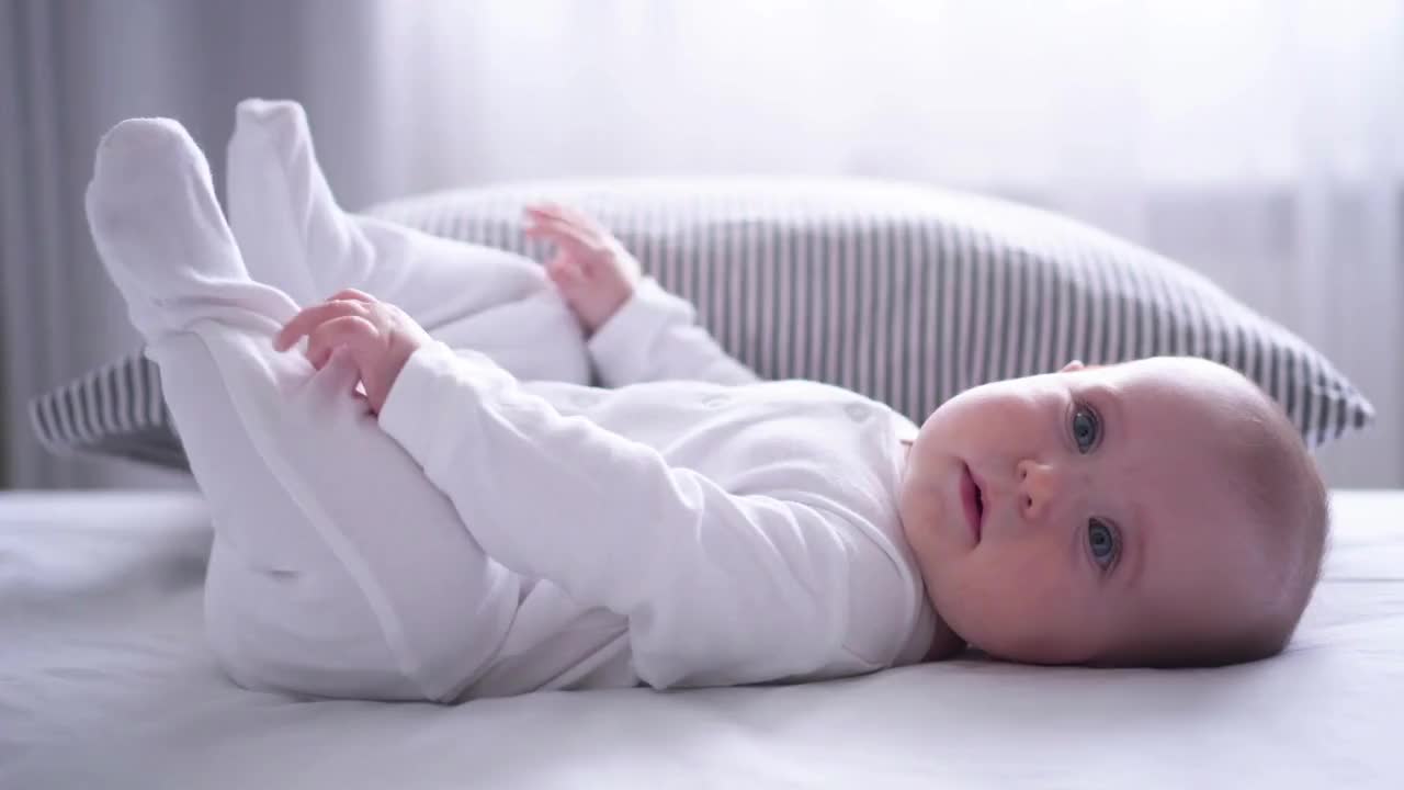 Funny chubby baby playing with feet on bed