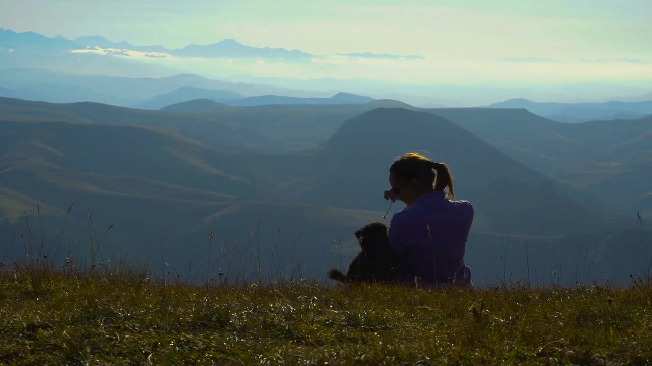 A gril caressing her dog in the mountains and looking wide on sunset