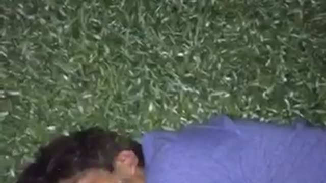 Guy in purple shirt gets drink poured on face while laying on grass instantly wakes up and runs