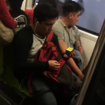 Man solves rubix cube with one hand on subway