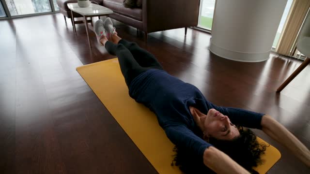 slow-motion footage of a woman exercising on a yoga mat in the living room floor