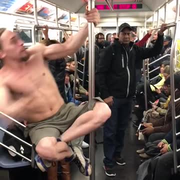 Shirtless man grey shorts dancing on pole subway