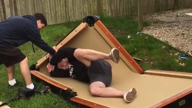 Barefoot guy jumps off wood balcony onto pool table