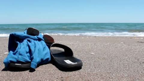 Flip-flops, T-shirt and glasses on the sand