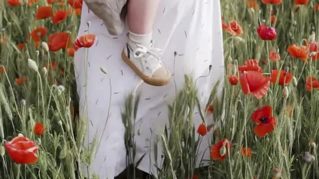 Mother walks on red poppy field while carrying her baby