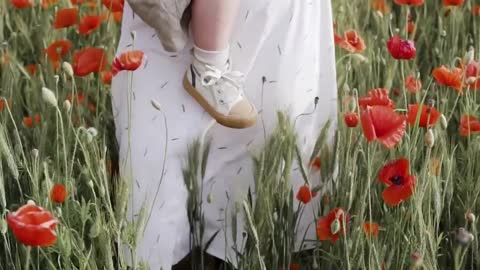 Mother walks on red poppy field while carrying her baby