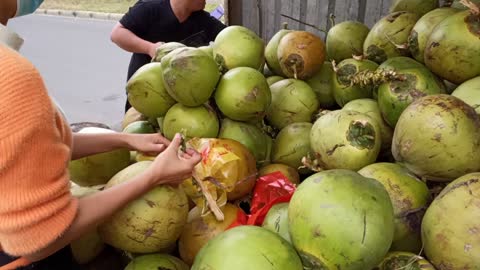 The coconut seller busting the coconut open with a knife.