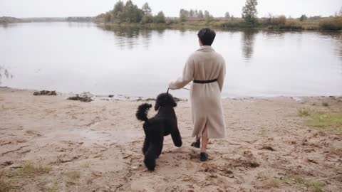 A young brunette in a white coat goes to the river and holds