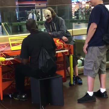Guy clown face mask watching guy play on orange yellow piano