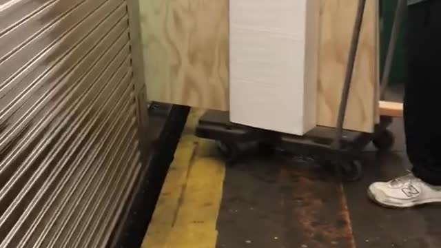 Guy trying to load big large piece of wood on cart onto subway train