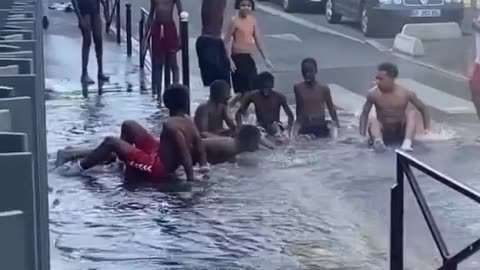 African migrants burst a fire hydrant to cool off for a while in a Paris.