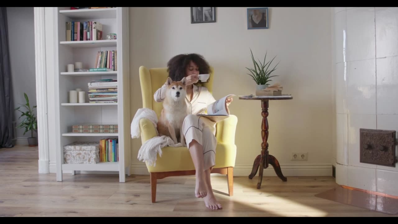 A Woman Having Coffee And Reading Magazine While Seated On A Chair With Her Dog