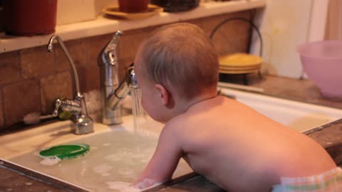 Baby boy drinking dirty dishwater in the kitchen.