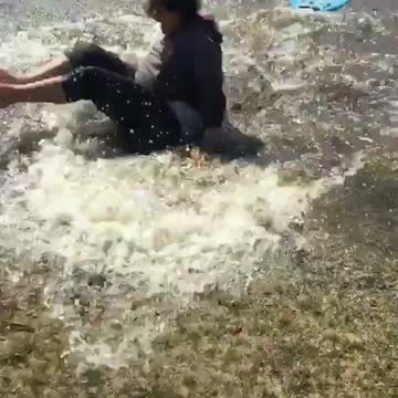 Grey shirt kid tries to boogie board across large puddle falls