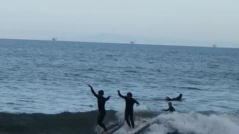 Two guys surfboarding smaller guy runs into other guy and falls into water