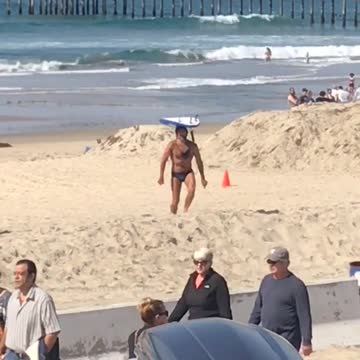 Guy in blue speedo balancing surfboard at beach