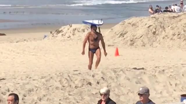 Guy in blue speedo balancing surfboard at beach