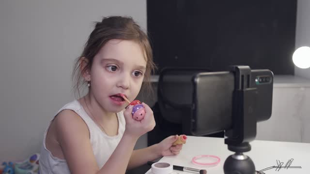 Little Girl Applying Lipstick While Looking At Her Smartphone