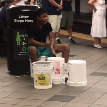 Guy in black shirt plays drums on buckets