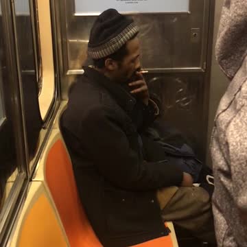 Man smokes in the corner seat on subway train