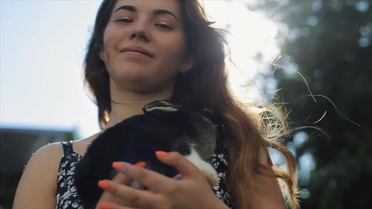 Pretty young girl standing in the sun with a little rabbit in her hand