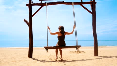 Woman swinging on a sunny beach, back view