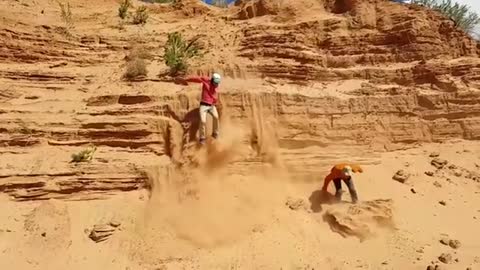 Two guys try to get down of a sand cliff - One fails