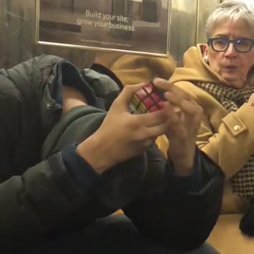 Guy does rubik's cube with head down without looking on subway train
