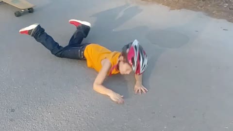 Little boy in yellow shirt helmet falls off skateboard